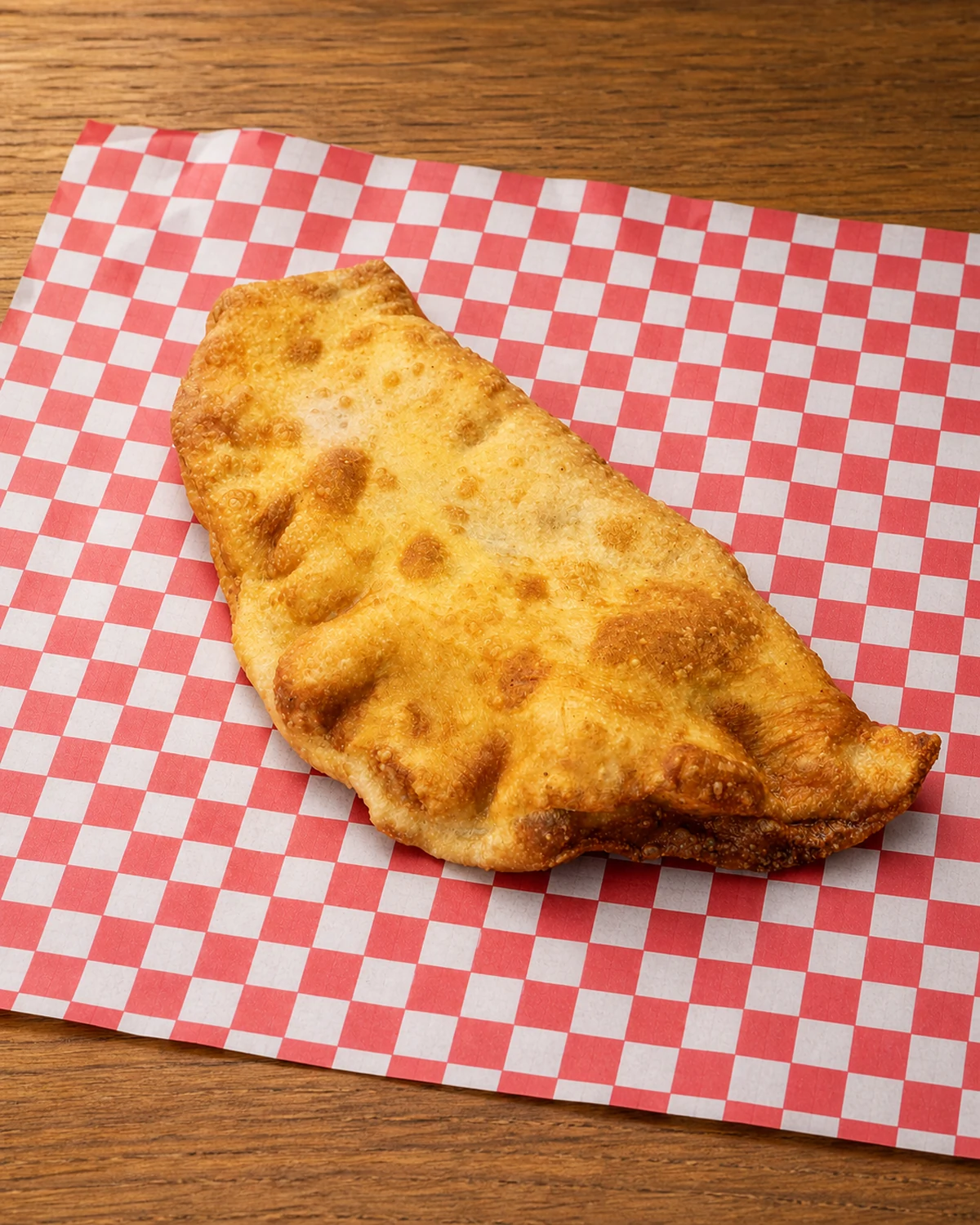 Whole golden fried classic calzone on red and white checkered paper
